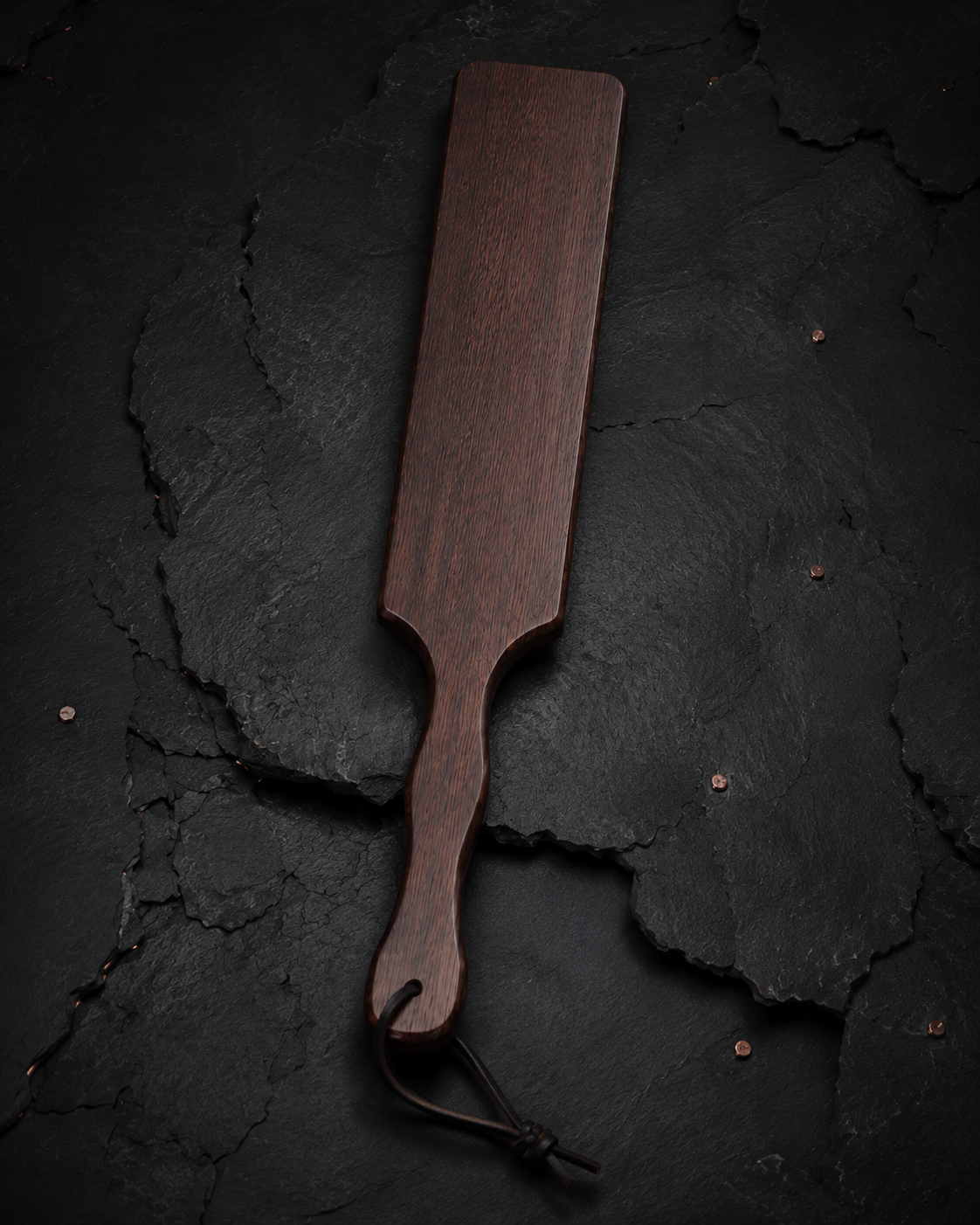 Full wooden discipline paddle on a dark archival surface