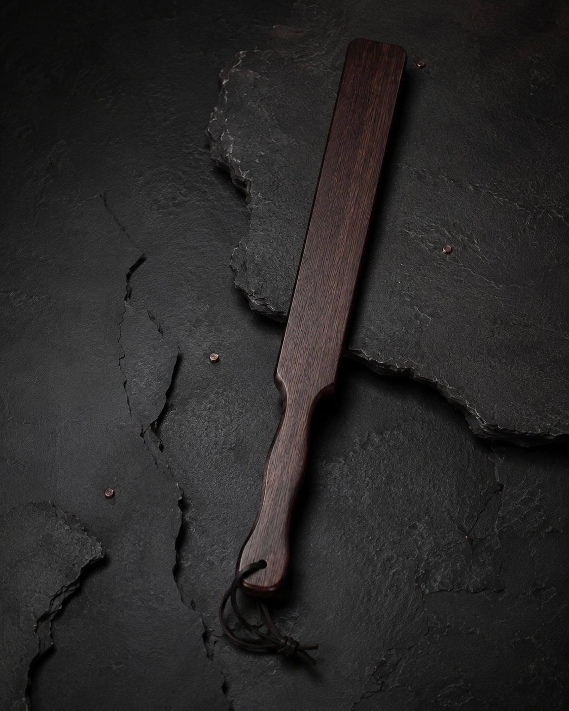 Slim wooden discipline paddle on a dark archival surface